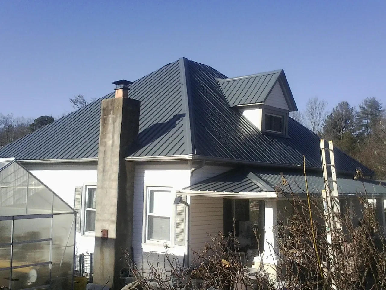 Dark blue standing seam metal roof on a white farmhouse with dormer — Slate & Tile Roof Repair by Roofing Brothers in Perkins