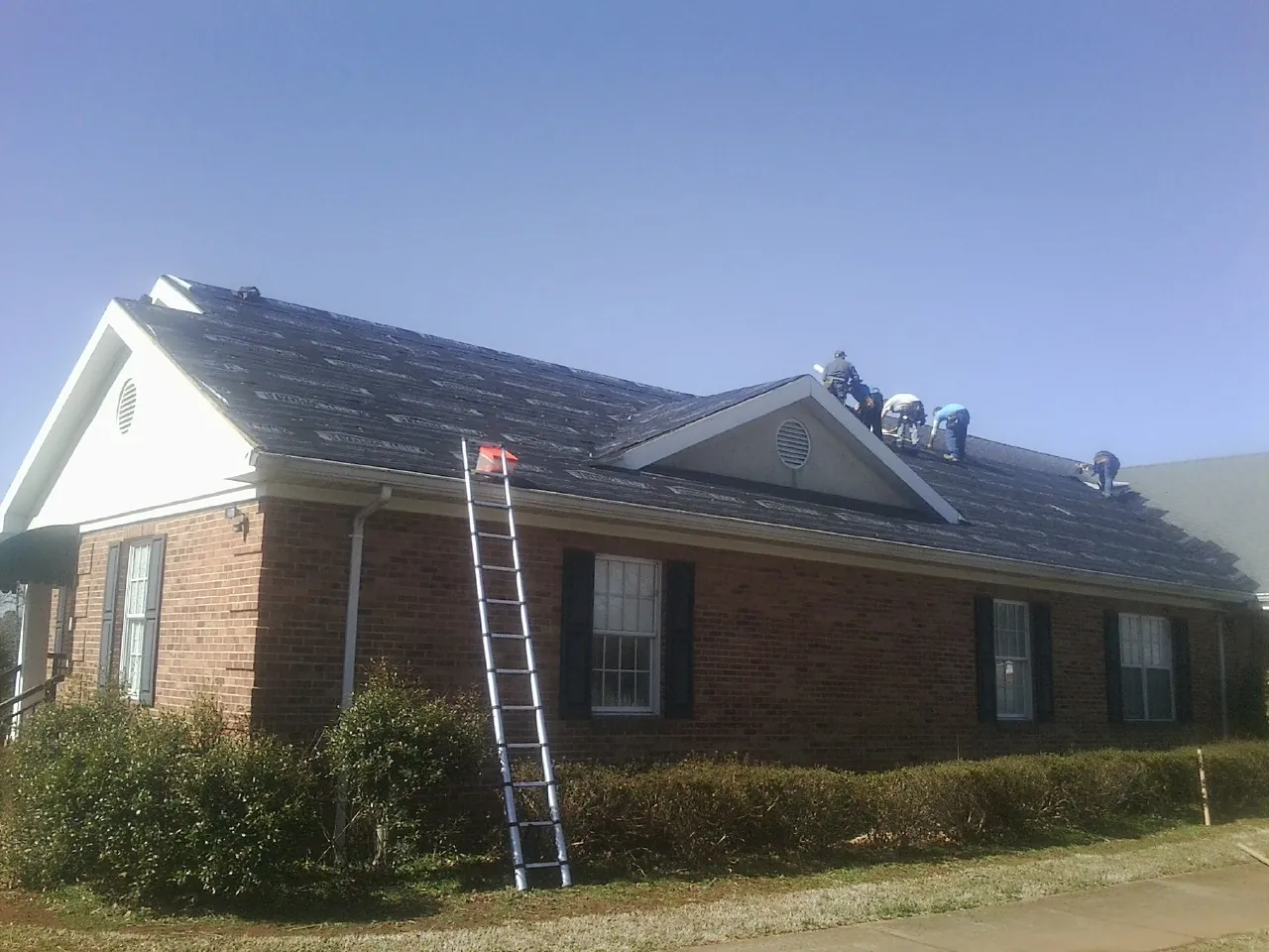 Crew tearing shingles off a brick ranch roof with a ladder set — Metal Roof Repair work by our crew in Perkins