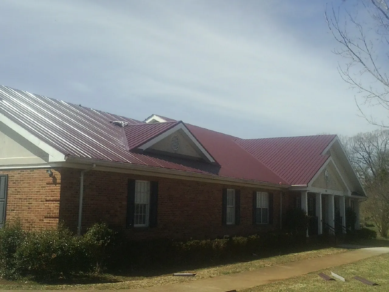 Red metal roof with gabled entries on a long brick building, from a Hail Damage Roof Repair job in Perkins