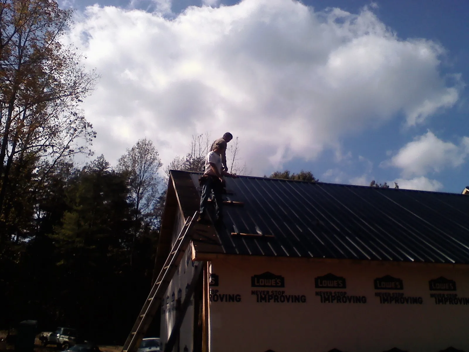 Roofer fastening dark metal panels high against a cloudy sky, from a Roof Inspection job in Perkins
