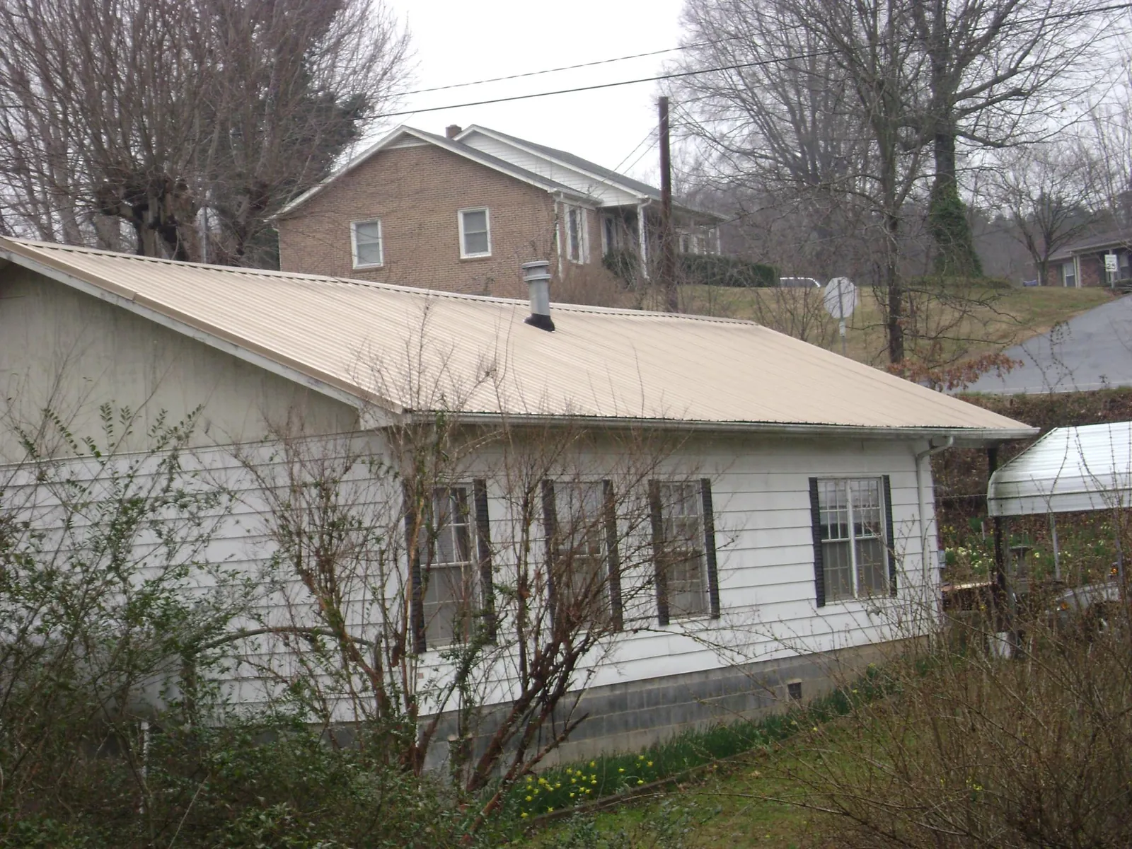 Tan metal roof on a white sided house set into a hillside — Commercial Roofing by Roofing Brothers in Perkins